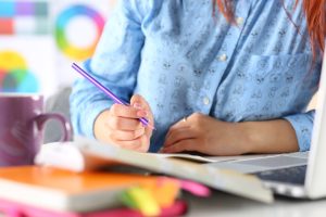 Female student, blogger or designer at workplace holding pencil and writing or making sketches. Woman writing letter, list, plan, making notes, doing homework. Education or creative work concept