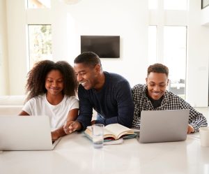 Smiling dad helping his teen kids with their homework, front view, close up