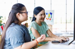 Portrait shot of Asian mother and daughter smiling at a computer.