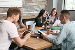 Two female and two male teenagers sit around a desk discussing schoolwork.