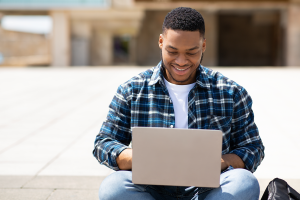 Male Black student smiles while working on laptop.