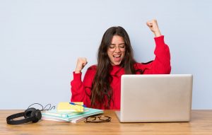 Female student celebrates in front of her laptop.